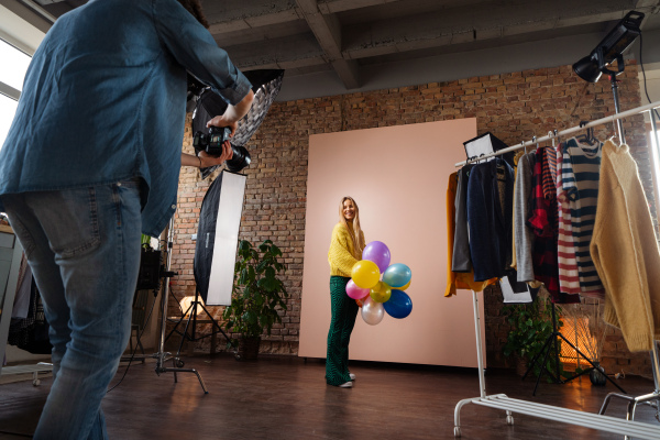 A fashion studio portrait of a happy young woman with balloons , backstage of photoshooting .