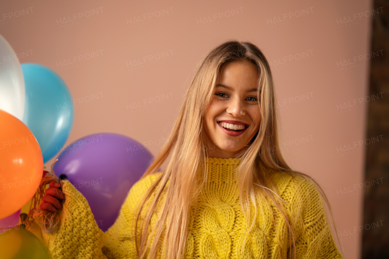 A studio portrait of a happy young blonde woman with balloon over pink background.