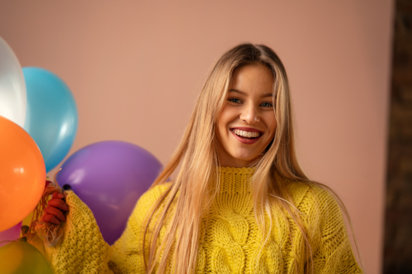 A studio portrait of a happy young blonde woman with balloon over pink background.