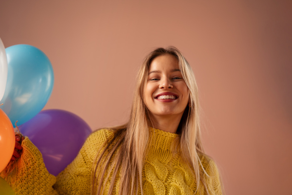 A studio portrait of a happy young blonde woman with balloons over pink background.