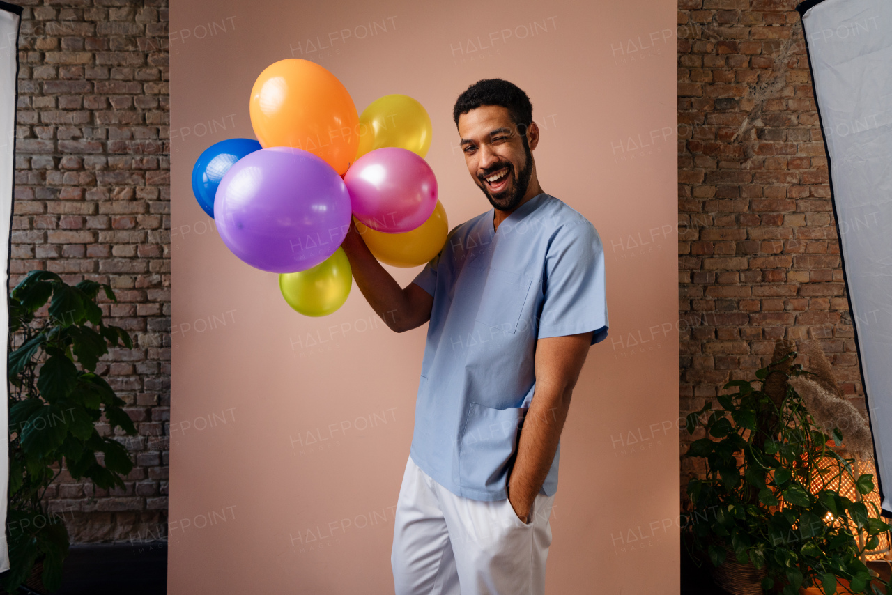 A happy young pediatrician holding balloons over pink background