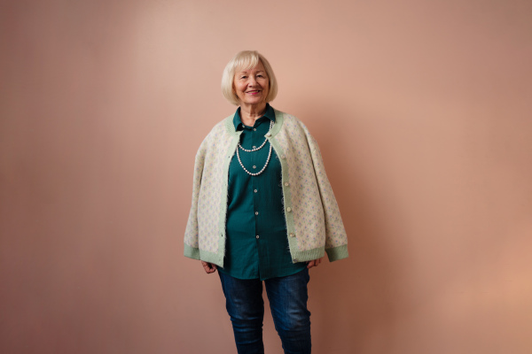 Senior woman posing after photoshooting day in front of a pink background.