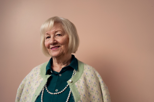 A smiling elegant elderly woman on pink color background, studio portrait