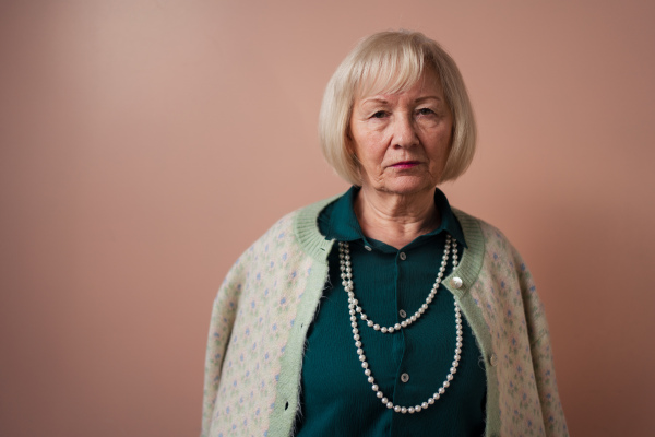 A sad elegant elderly woman on pink color background, studio portrait