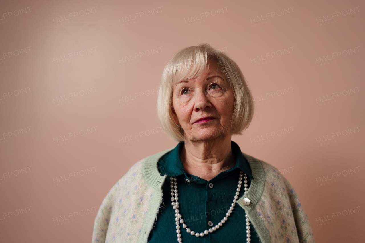 A sad elegant elderly woman on pink color background, studio portrait