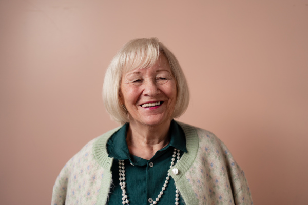 A smiling elegant elderly woman on pink color background, studio portrait