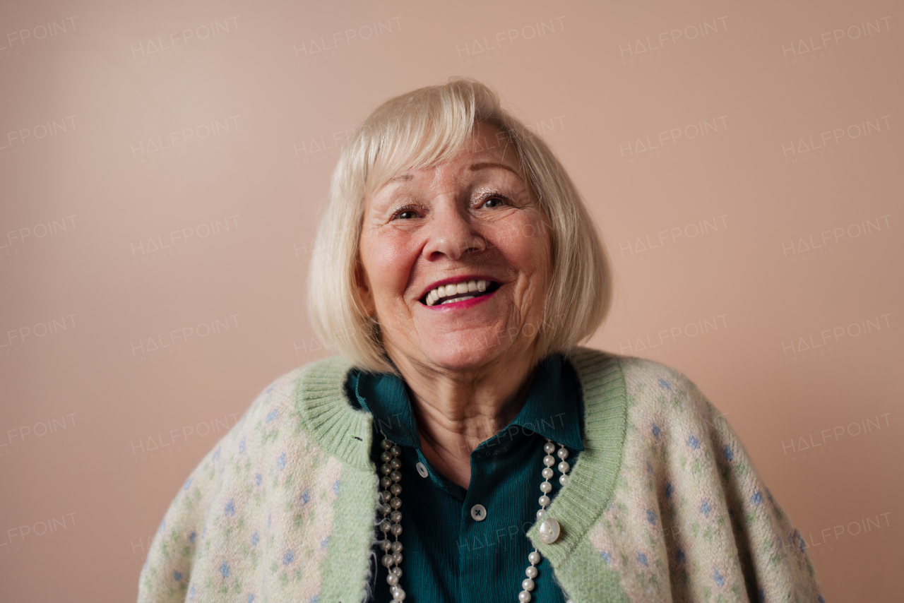 A smiling elegant elderly woman on pink color background, studio portrait