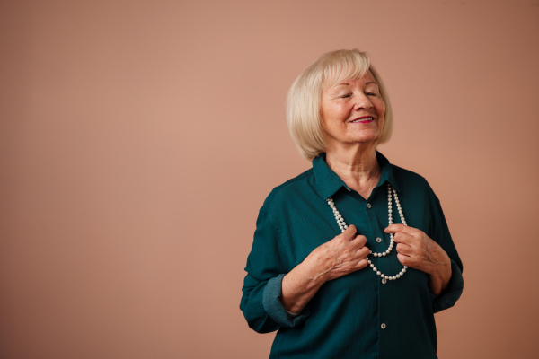 A smiling elegant elderly woman with pearls on pink color background, studio portrait