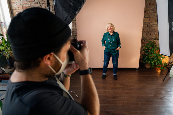 A young photographer taking picures of elderly woman, backstage of photoshooting in studio.