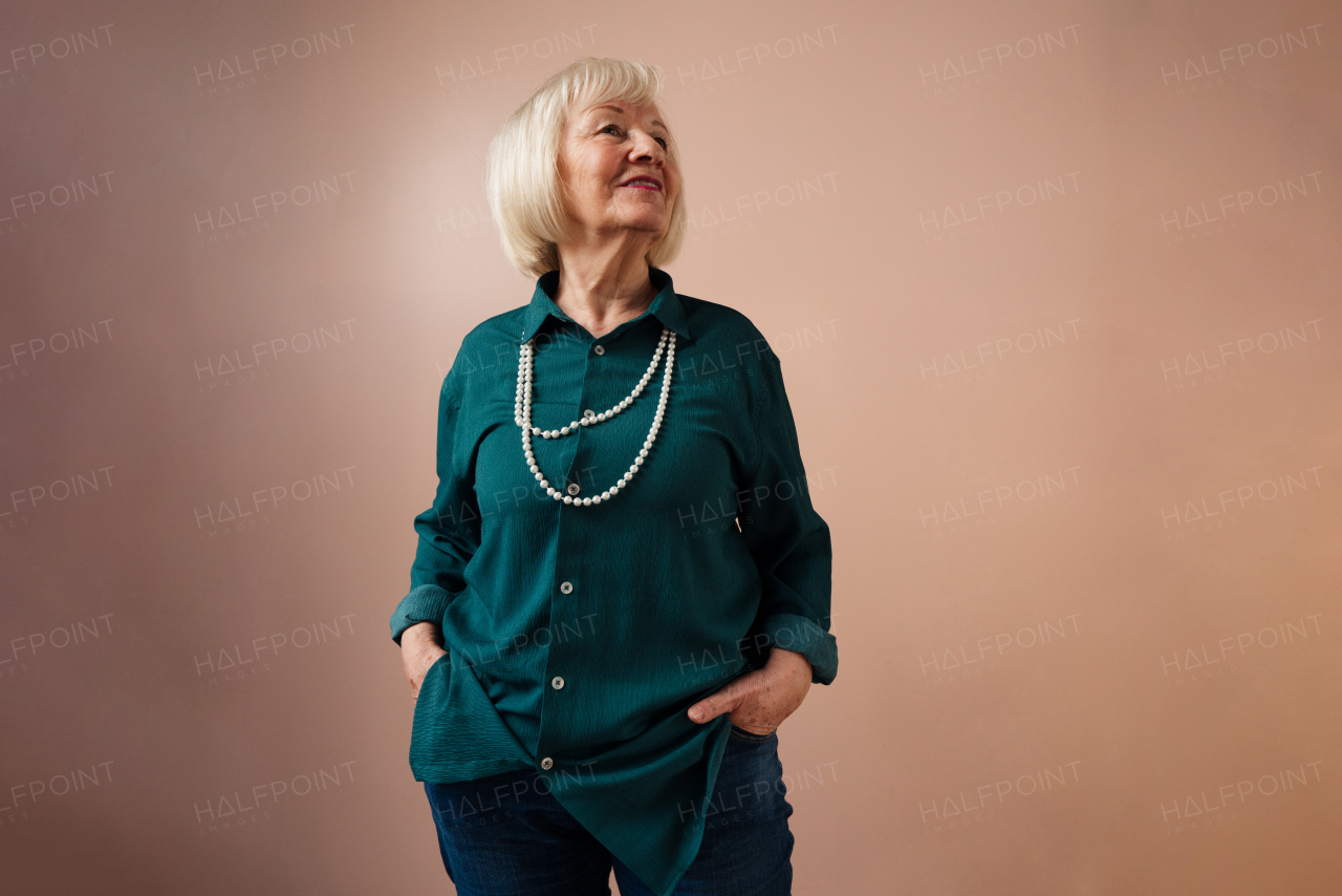 A smiling elegant elderly woman on pink color background, studio portrait