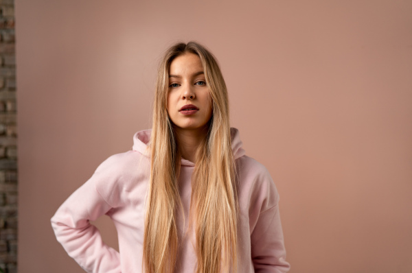 A fashion studio portrait of a happy young blonde woman in hoodie posing over pink background.