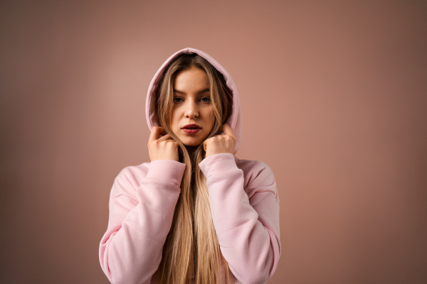 A fashion studio portrait of a happy young blonde woman in hoodie posing over pink background.