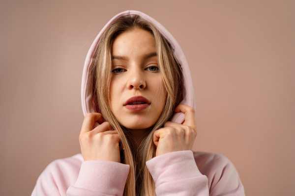 A fashion studio portrait of a happy young blonde woman in hoodie posing over pink background.