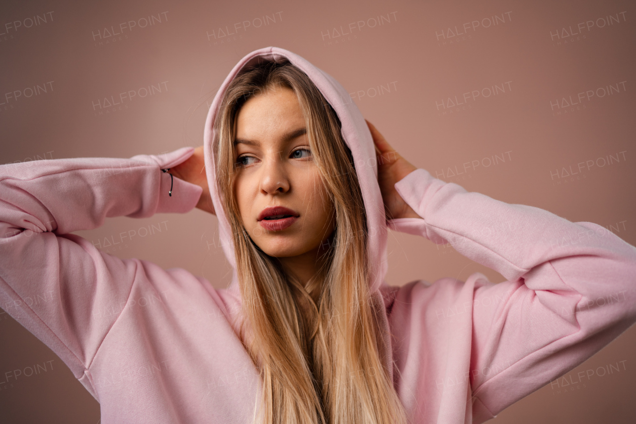 A fashion studio portrait of a happy young blonde woman in hoodie posing over pink background.