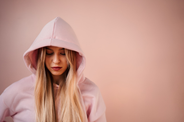 A fashion studio portrait of a happy young blonde woman in hoodie posing over pink background.