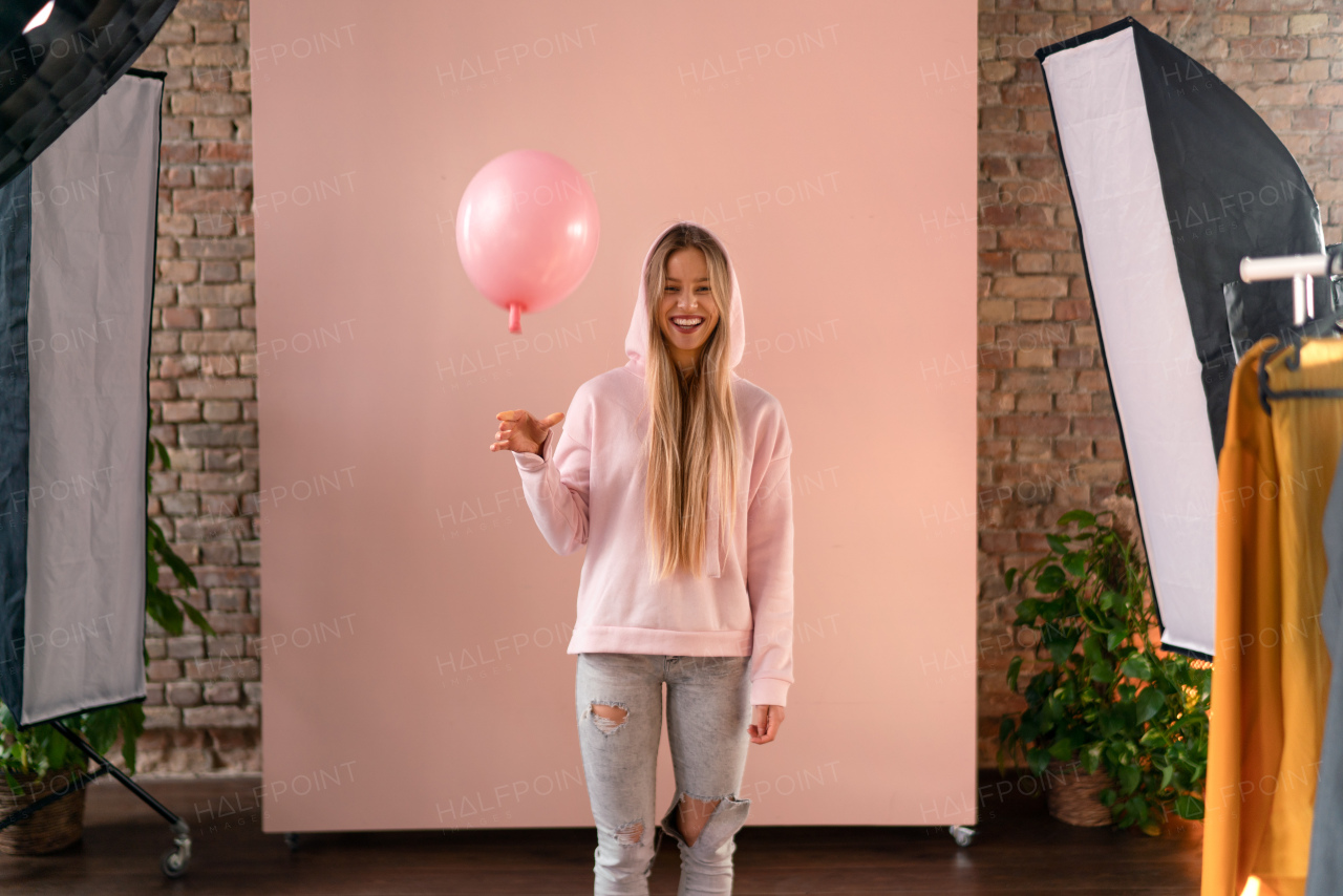 A studio portrait of a happy young blonde woman with balloon over pink background.