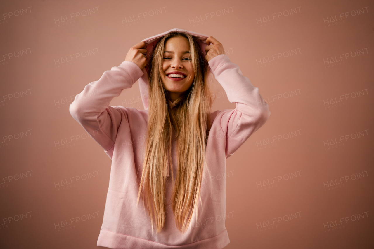 A fashion studio portrait of a happy young blonde woman in hoodie posing over pink background.