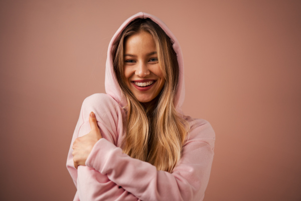 A fashion studio portrait of a happy young blonde woman in hoodie posing over pink background.