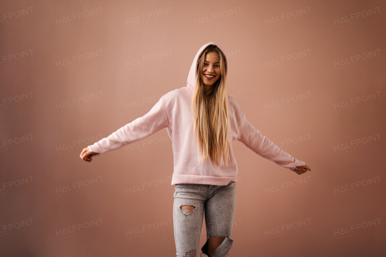 A fashion studio portrait of a happy young blonde woman in hoodie posing over pink background.