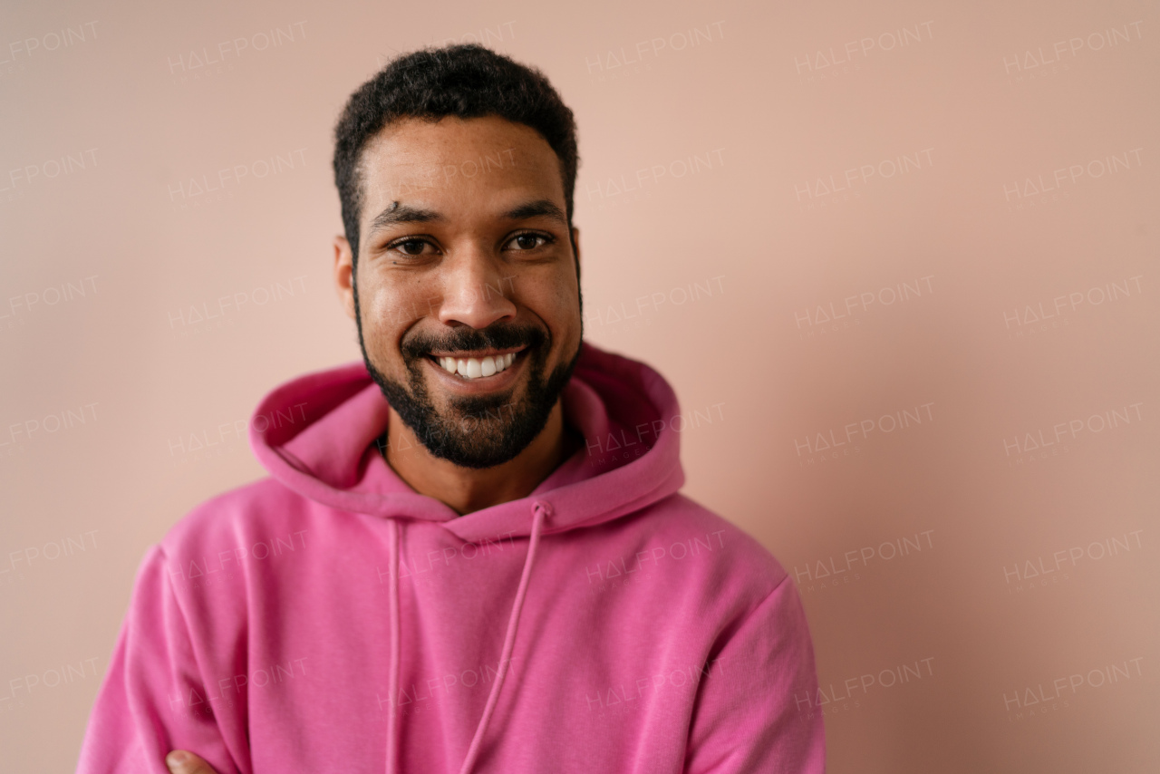 A fashion studio portrait of a young African American man in pink hoodie posing over beige background.