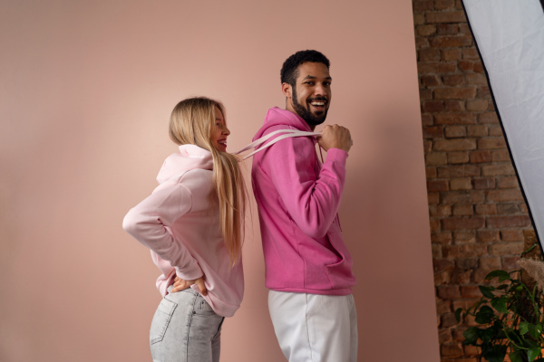 A fashion studio portrait of a happy young blonde woman in hoodie posing over pink background.