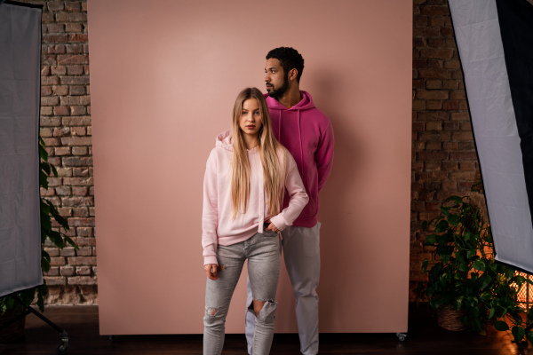 A fashion studio portrait of a happy young blonde woman in hoodie posing over pink background.