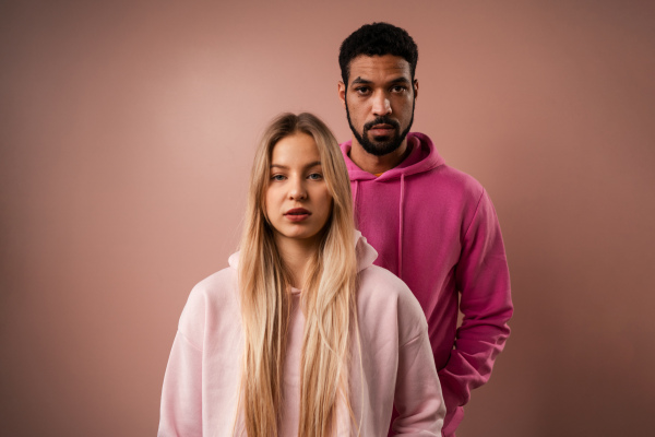 A fashion studio portrait of a happy young blonde woman in hoodie posing over pink background.