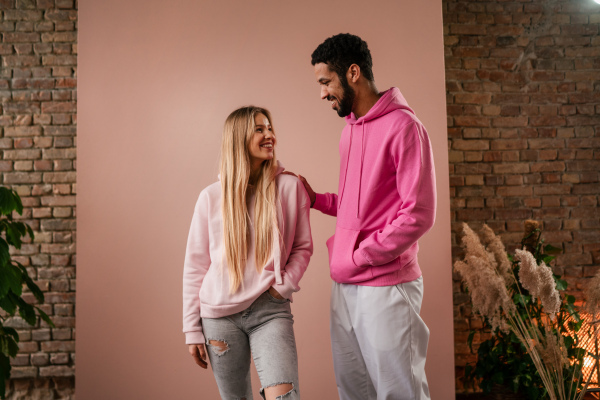 A fashion studio portrait of a happy young blonde woman in hoodie posing over pink background.