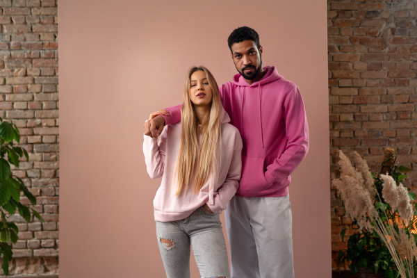 A fashion studio portrait of a happy young blonde woman in hoodie posing over pink background.