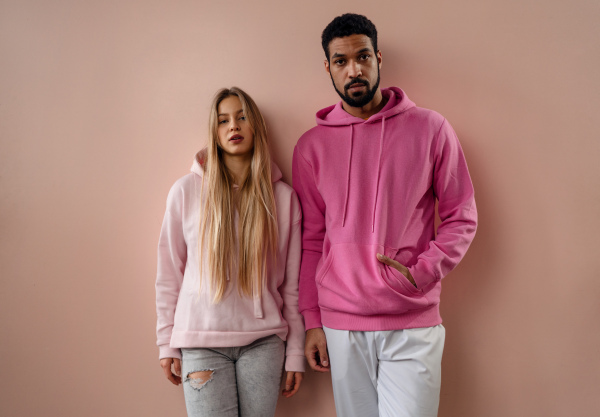 A fashion studio portrait of a happy young blonde woman in hoodie posing over pink background.