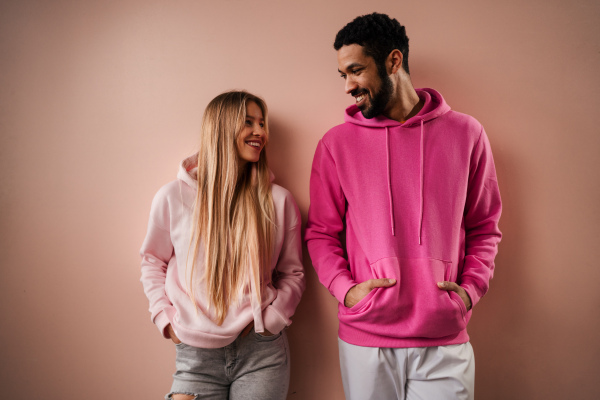 A fashion studio portrait of a happy young blonde woman in hoodie posing over pink background.