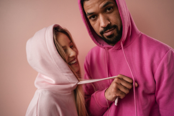 A fashion studio portrait of a happy young blonde woman in hoodie posing over pink background.