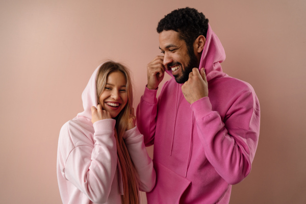 A fashion studio portrait of a happy young blonde woman in hoodie posing over pink background.