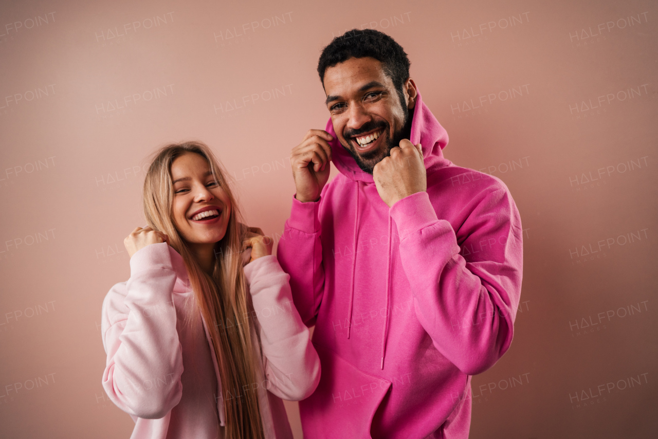 A fashion studio portrait of a happy young blonde woman in hoodie posing over pink background.