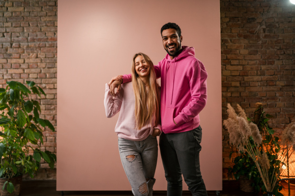 A fashion studio portrait of a happy young blonde woman in hoodie posing over pink background.