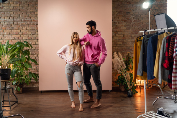 A fashion studio portrait of a happy young blonde woman in hoodie posing over pink background.