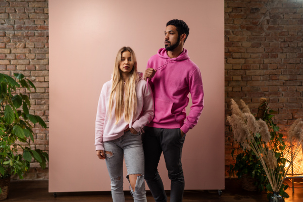 A fashion studio portrait of a happy young blonde woman in hoodie posing over pink background.