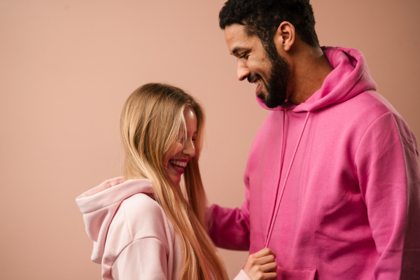 A fashion studio portrait of a happy young blonde woman in hoodie posing over pink background.