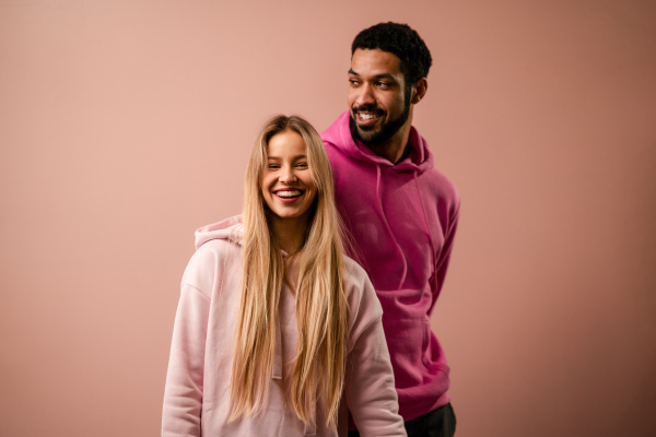 A fashion studio portrait of a happy young blonde woman in hoodie posing over pink background.