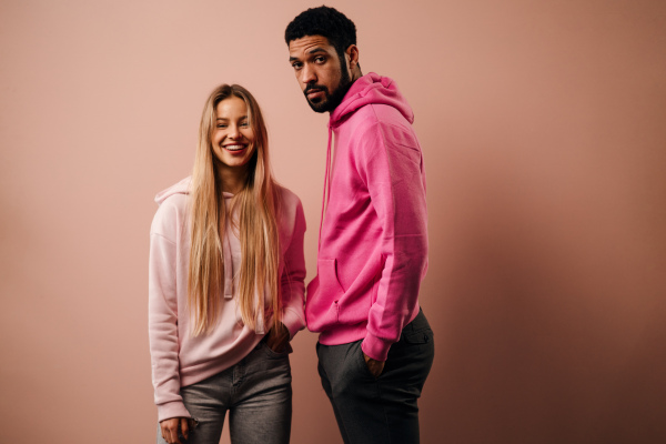 A fashion studio portrait of a happy young blonde woman in hoodie posing over pink background.