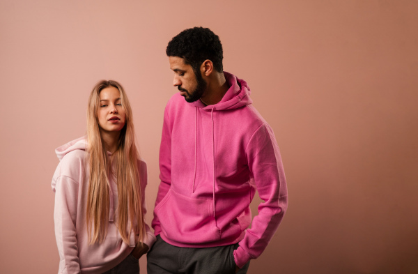 A fashion studio portrait of a happy young blonde woman in hoodie posing over pink background.