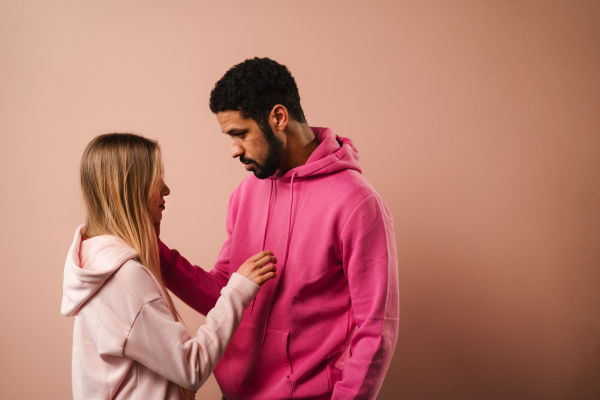 A fashion studio portrait of a happy young blonde woman in hoodie posing over pink background.