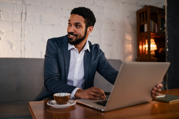 A happy young businessman having coffee and doing his work in cafe.