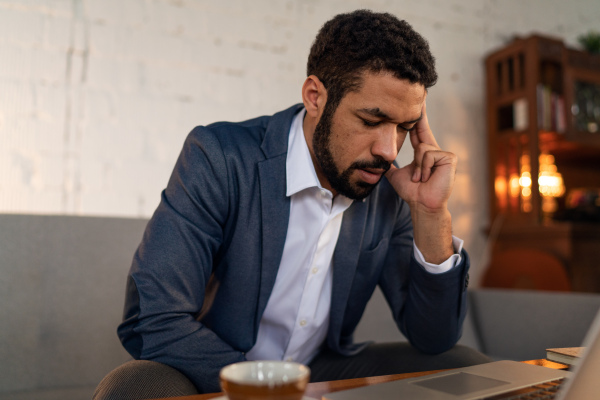 An overworked young businessman suffering from headache in modern home office with laptop on desk