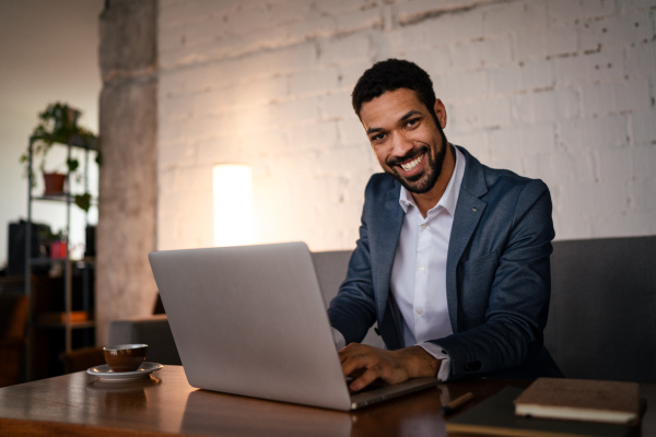 A happy young businessman having coffee and doing his work in cafe.