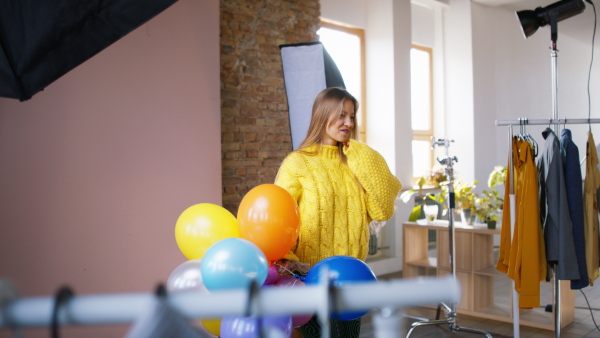 A fashion studio shooting of a happy young woman with balloons , backstage of photoshooting .