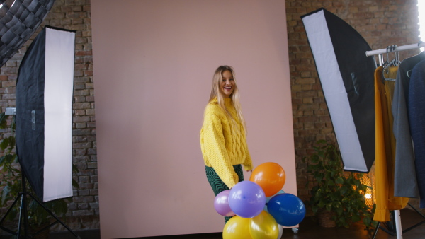 A fashion studio shooting of a happy young woman with balloons , backstage of photoshooting .