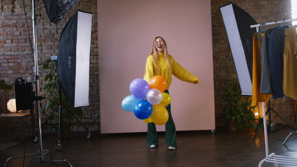 A fashion studio shooting of a happy young woman with balloons , backstage of photoshooting .