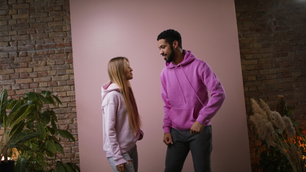 A fashion studio shooting of a happy young couple in hoodie posing over pink background.