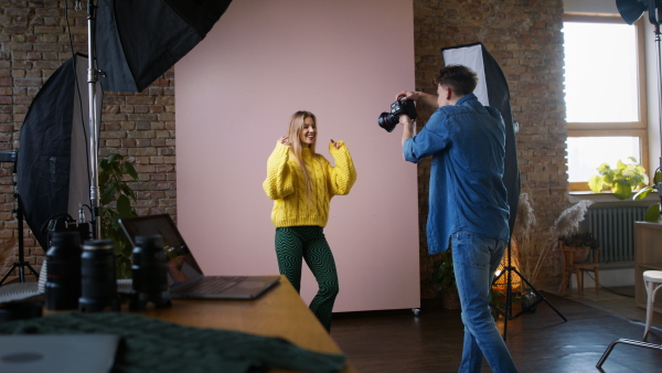 A young photographer taking picures of model, backstage of photoshooting in studio.